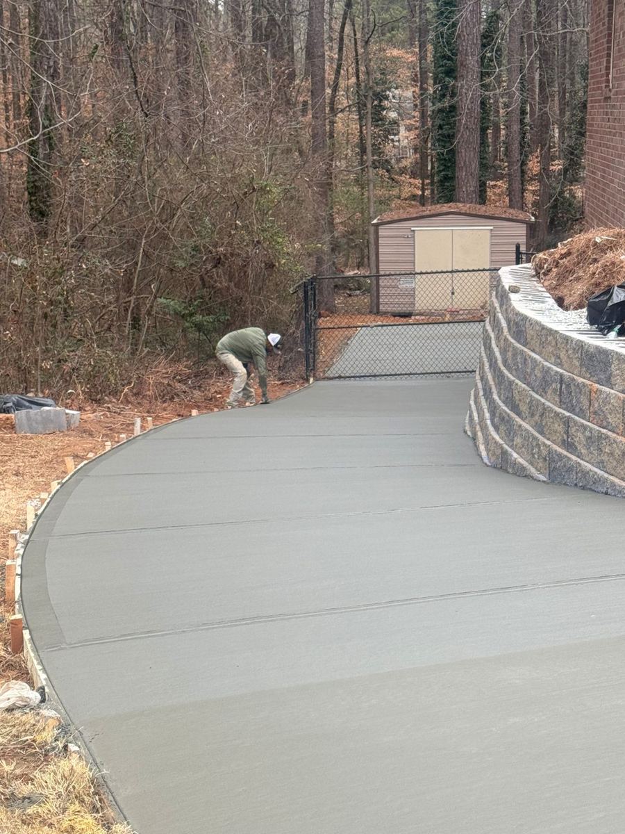 Crew finishing a freshly poured curved concrete driveway beside a block retaining wall in Gwinnett County, GA