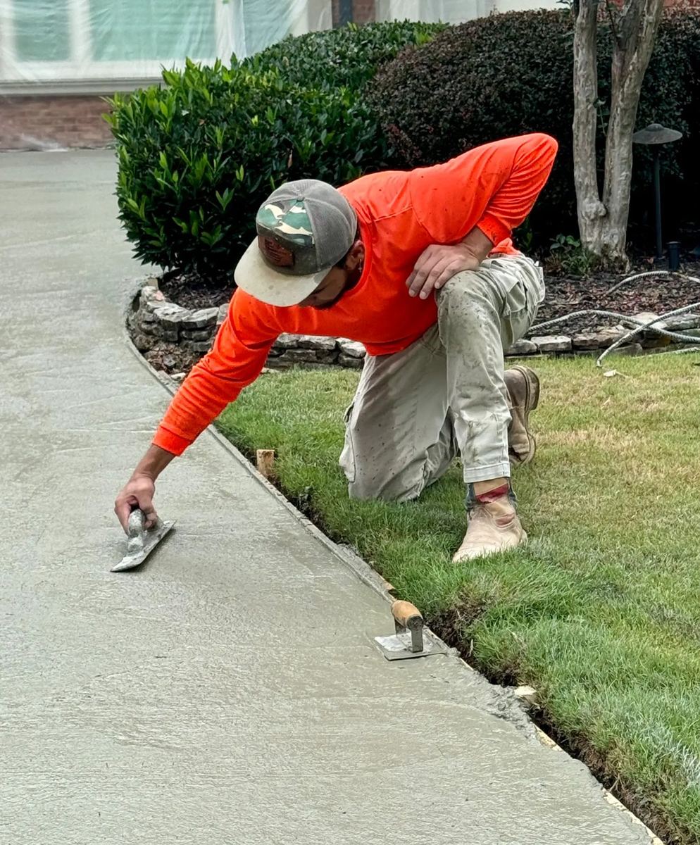 Crew member hand-edging fresh concrete driveway next to a green lawn in Gwinnett County, GA
