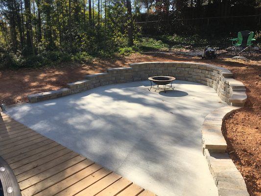 Concrete patio with a curved seat wall and fire pit next to a wood deck in Gwinnett County, GA
